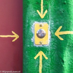 Foto een gele deurbel op een groene achtergrond (en vier pijlen).