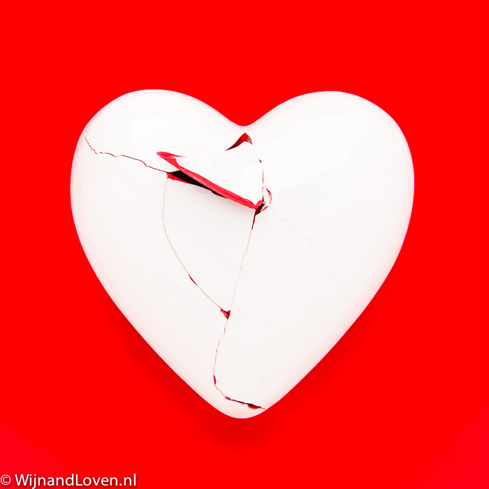 Conceptfoto gebroken hart - wit porseleinen hart met scheuren op rode achtergrond